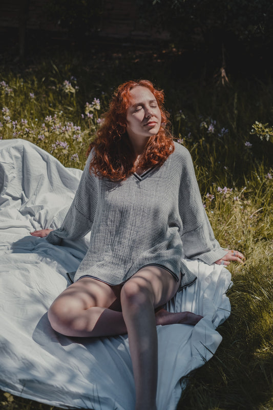 Eine rothaarige Frau mit geschlossenen Augen sitzt auf einer Decke und wirkt entspannt.