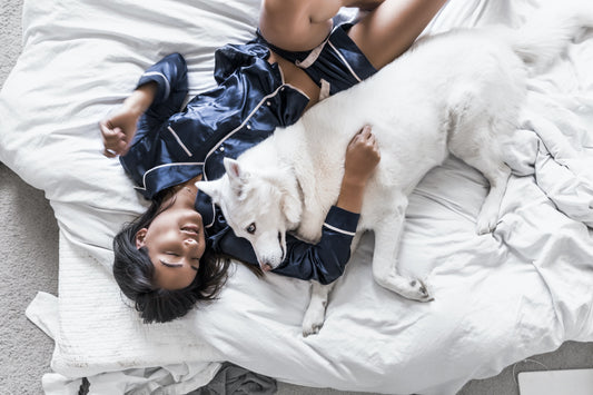Eine Frau in einem Pyjama liegt entspannt im Bett und kuschelt mit ihrem weißen Hund.