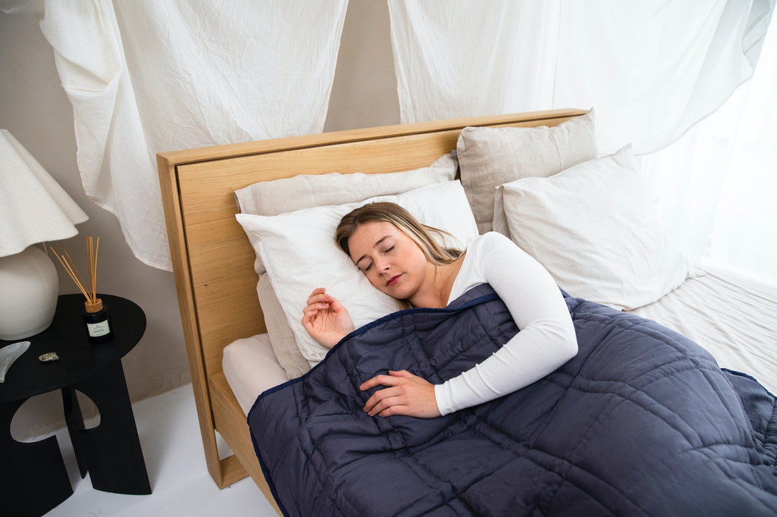 Eine blonde Frau liegt entspannt im Bett mit geschlossenen Augen, eingehüllt in eine gemütliche Bettdecke.